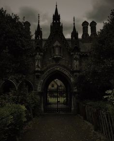 an old building with a gate in front of it and dark clouds above the buildings