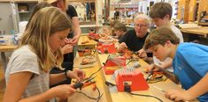 several people are working on electronic devices in a workshop with two boys and one girl