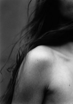 a black and white photo of a woman's back with her hair blowing in the wind