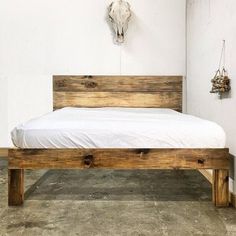 a wooden bed frame with white sheets on it and a cow skull mounted to the wall