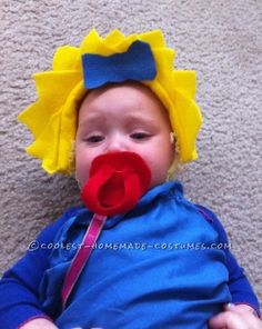 a baby wearing a yellow and red clown nosepiece laying on the floor next to a carpet