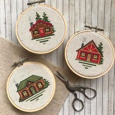 two cross - stitch hoops with houses and trees on them, one is holding a pair of scissors