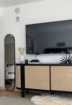 a flat screen tv sitting on top of a wooden cabinet in a living room next to a large mirror