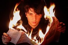 a young man holding a book in front of his face with flames coming out of it