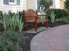 a wooden bench sitting in the middle of a garden next to a brick walkway and shrubbery