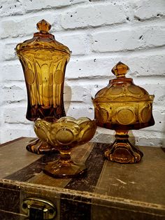 two glass vases sitting on top of an old suitcase next to a brick wall