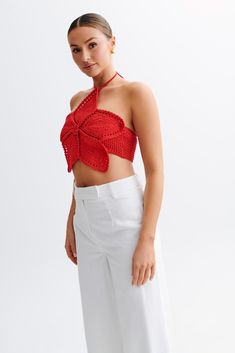 a woman wearing white pants and a red crop top with an open back, standing in front of a white background