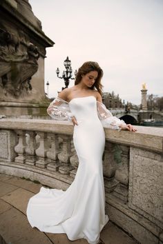 a woman in a white dress leaning against a wall with her arms on the railing