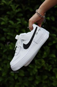 a person is holding up a white nike air force shoe with black swarongs on it