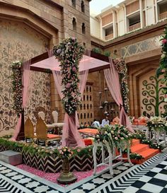 an outdoor wedding setup with pink drapes and flowers on the bed, in front of a building