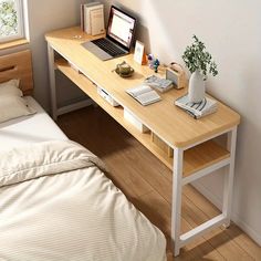 a laptop computer sitting on top of a wooden desk next to a bed with white sheets