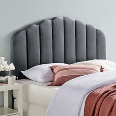 a gray headboard with pink and white pillows on it next to a bed in a bedroom