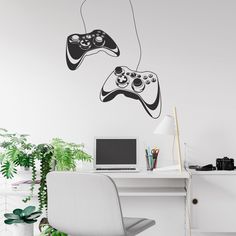 two video game controllers are hanging on the wall above a desk with a laptop and potted plant