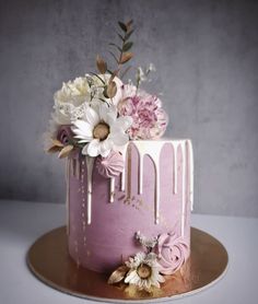 a pink cake with white flowers and icing drips on the top is sitting on a gold plate