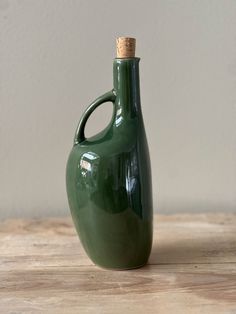 a green vase sitting on top of a wooden table next to a corked bottle