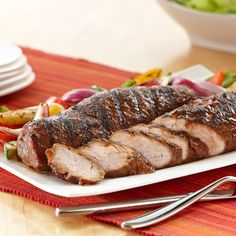 a large piece of meat on a plate next to some salads and silverware