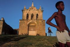 a young boy standing in front of an old building with a cross on it's side