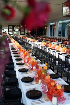 a long table is set up with black plates and orange centerpieces for an event