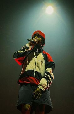 a man standing on top of a stage wearing a red and black jacket with his hands in his mouth