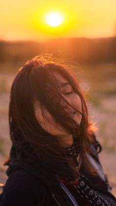 a woman with long hair standing in front of the sun and looking at her cell phone