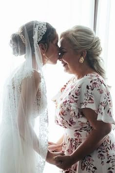 two brides kissing each other in front of a window with the veil pulled back