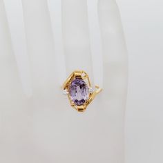 a hand holding a ring with a large purple stone in the center and two small white diamonds on each side