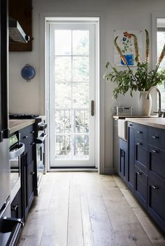 a kitchen with wooden floors and white walls, an open door leading to the outside