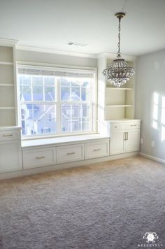 an empty living room with built in bookcases and a chandelier hanging from the ceiling