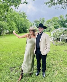 a man and woman in cowboy hats posing for a photo on the grass with trees behind them