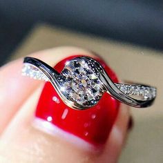 a woman's hand holding a diamond ring on top of a red manicured nail