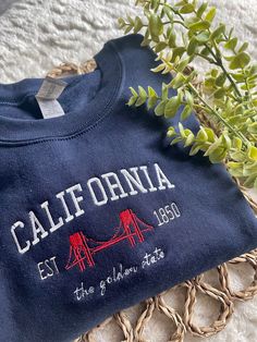 Cali, stand up! Comfy sweatshirt with California in a varsity-like font featuring the Golden Gate Bridge. This pullover Crewneck will keep you stylish and cool! You can add names on the sleeve for $5 extra!  This sweatshirt is available in 6 colors:  ✨ Forest Green ✨ Sand ✨ White ✨ Light Blue ✨ Navy  ✨ Heather Gray If there is a color you have in mind other than the ones available, send me a message and I can help! -Sweatshirt brand: Gildan -Sizes available: Adult Small - Adult 3XL -Fit: slightl Crew Neck T-shirt With Letter Embroidery For College, College Crew T-shirt With Embroidered Text, Varsity Style Campus Top With Letter Embroidery, College Style Sweatshirt With Letter Embroidery, College T-shirt With Letter Embroidery, Crew T-shirt With Letter Embroidery For College, College Crew T-shirt With Letter Embroidery, Crew Neck Top With Embroidered Text For College, Embroidered Text Crew Neck Top For School