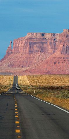 a truck driving down the road in front of a large rock formation with mountains behind it