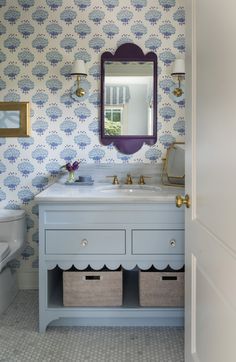 a bathroom with blue and white wallpaper, gold accents and purple mirror above the sink