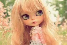 a close up of a doll with long blonde hair and blue eyes wearing a dress