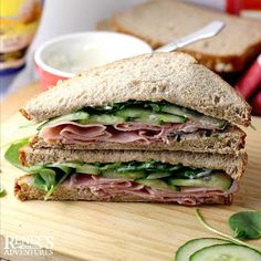 a cut in half sandwich sitting on top of a cutting board next to cucumber slices