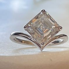 an engagement ring with a princess cut diamond in the center, on a white surface