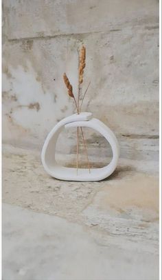 a white vase sitting on top of a stone wall next to a plant in it