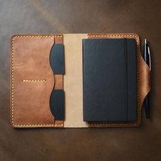 a notebook and pen sitting on top of a brown leather cover covered in stitching