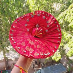 a person holding up a red fan in front of some trees and cars on the street