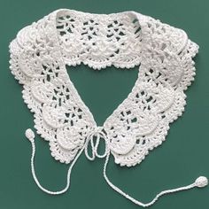 a white crocheted lace collar on a green surface with a string attached to it