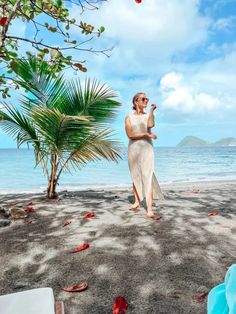 a woman standing on top of a sandy beach next to the ocean and palm trees