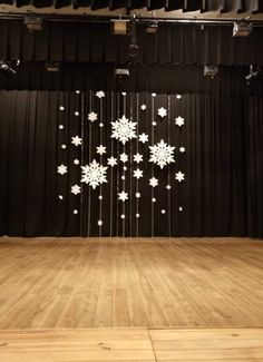 an empty stage with black curtains and snowflakes hanging from the ceiling in front of it