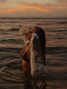 a woman standing in the water with her arms around her head, wearing a sheer white top