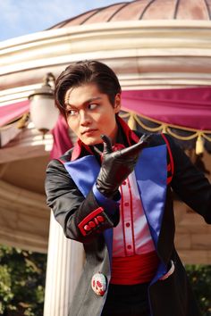 a man dressed in costume pointing at something with his hand and wearing gloves while standing next to a gazebo