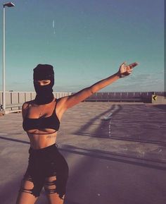 a woman wearing a black outfit and mask on top of a parking lot with her arms outstretched