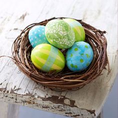 four painted eggs in a bird's nest on an old wooden table with white paint