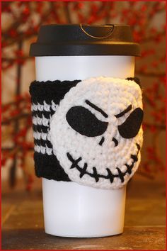 a knitted coffee cup cozying with a skull on the front and black bottom