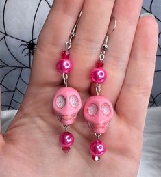 a pair of pink earrings with skulls and pearls on them are being held by a hand