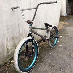 a bike with blue rims parked next to a white wall and cement block behind it