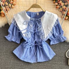 Add a touch of vintage charm to your wardrobe with this delightful blue gingham blouse, featuring intricate lace trims and a classic sailor collar. The blouse showcases a timeless gingham pattern in a fresh blue and white color palette, perfect for a chic and casual look. The oversized sailor collar is adorned with delicate lace detailing, adding a feminine and whimsical touch to the design.The blouse is designed with puff sleeves that have elasticized cuffs, creating a playful and comfortable f Blue Lace Collar Top For Summer, Retro Gingham Blouse For Spring, Spring Retro Gingham Blouse, Blue Short Sleeve Blouse With Lace Trim, Blue Doll Collar Top For Spring, Spring Tops With Lace Trim And Cute Collar, Spring Blouse With Lace Trim And Cute Collar, Blue Ruffled Tops For Picnic, Summer Doll Collar Top With Lace Trim